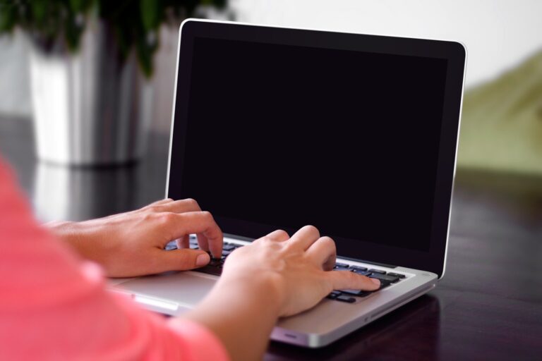 Person typing on a modern laptop keyboard with a dark screen